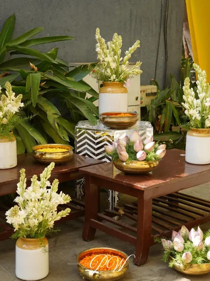 A close-up of the Haldi decor, featuring brass pots filled with turmeric and fresh white and pink flowers, blending tradition with soft aesthetics.