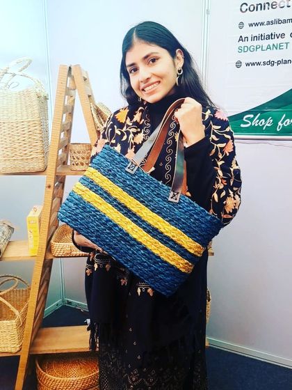 A customer showcasing our striped blue and yellow tote bag, made from woven natural fibers with durable leather-style straps. This spacious and stylish bag is perfect for work, shopping, or as a chic everyday carryall.