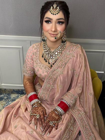 A beautiful bride in a pastel pink saree, wearing a heavy polki and black bead necklace set.