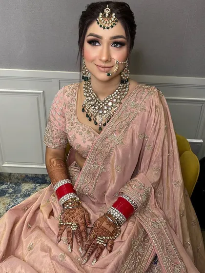 A beautiful bride in a pastel pink saree-lehenga, wearing a heavy polki set with black beads for a modern, contrasting look.