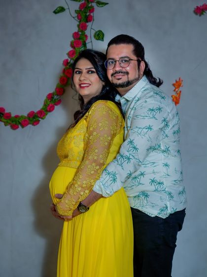 A classic couple's pose in a studio setting. The partner stands behind, protectively holding the baby bump, creating a portrait that is both traditional and full of love.