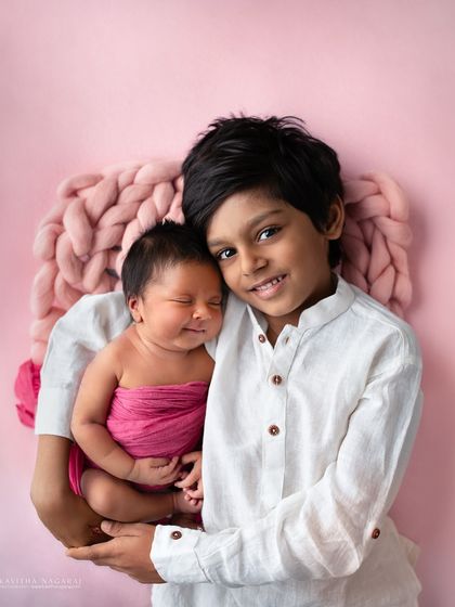 A big brother holds his smiling newborn sister. Her sweet expression and his gentle hold create a heartwarming and unforgettable sibling portrait.