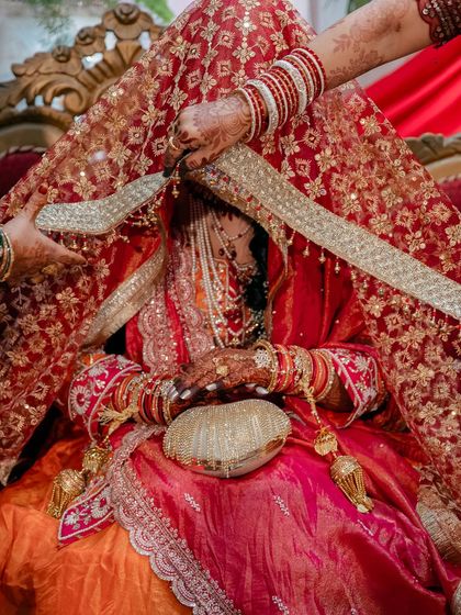 The bride being prepared for the ceremony, with hands adjusting her ornate red and gold veil. This behind the scenes moment is full of anticipation.