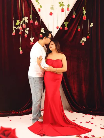A full-length portrait of the expecting couple in a tender embrace. The mother's red gown and the romantic Valentine's setup create a beautiful and memorable maternity photograph.