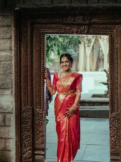 A bride in a stunning red saree, framed by an antique doorway, a classic and powerful bridal portrait.
