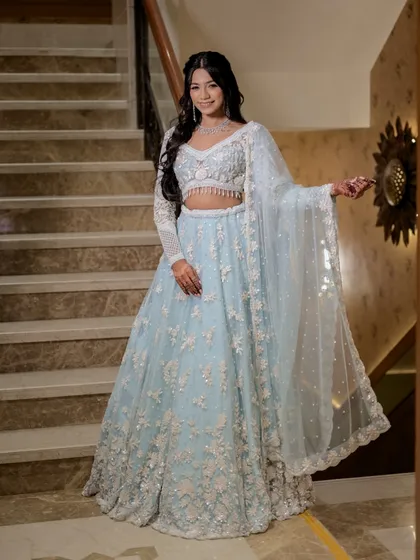 A stunning full-length portrait of the bride on a staircase. Her elegant pose and smile showcase the beautiful details of her powder blue embroidered lehenga.