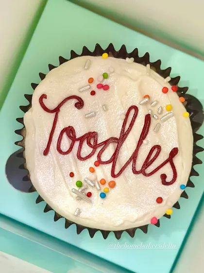 A close-up of one of our "Toodles" farewell cupcakes. You can see the smooth vanilla buttercream, the hand-piped message in red, and the mix of silver and rainbow sprinkles that add a bit of sparkle.