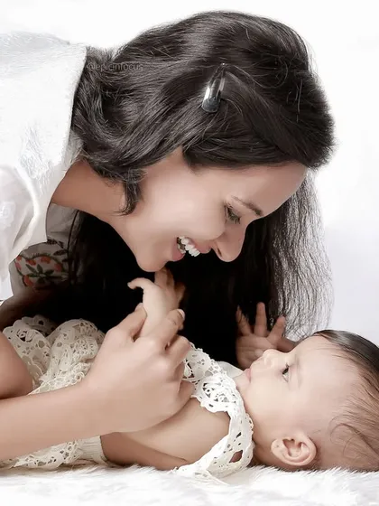 A mother and her baby share a playful moment on a soft white rug. Our studio provides a comfortable space for these natural, candid interactions.