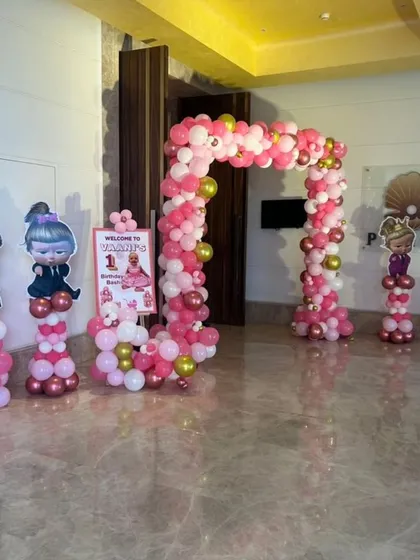 A "Boss Baby" themed entrance for a first birthday, with character cut-outs on balloon pillars and a pink and gold balloon arch.