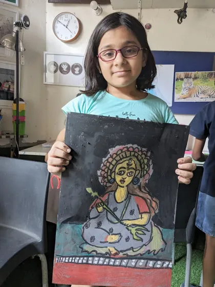 A student proudly displays her finished artwork inspired by traditional Indian art. In my drawing and painting sessions, we explore different mediums like oil pastels to bring vibrant cultural themes to life.