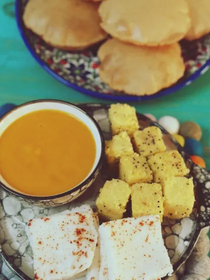 A perfect homemade Gujarati meal featuring sweet Aam Raas (mango pulp), fluffy puris, and savory white and yellow dhokla. This is the taste of summer and comfort, made fresh in our kitchen.