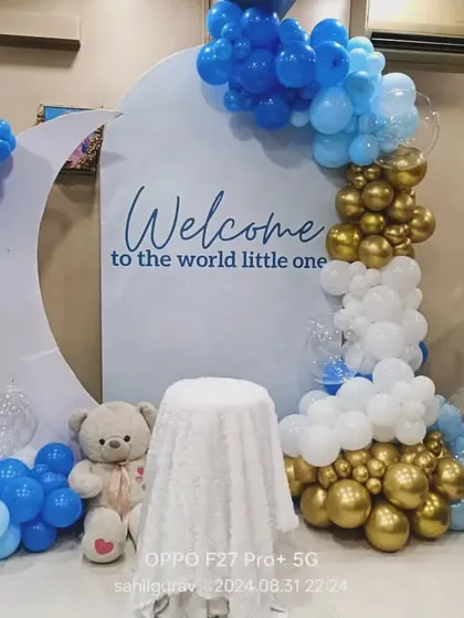 A classic blue, white, and gold balloon arrangement to welcome a little one into the world. This setup includes a moon backdrop, a small teddy bear, and 'BABY' blocks, making it a perfect surprise.