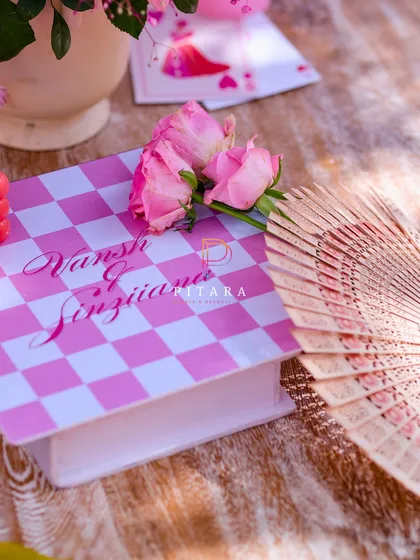 A custom-printed book box with the couple's names, paired with a vintage fan and fresh roses, serving as a unique decor element.
