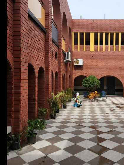 A wide view of the school courtyard, showing the combination of brick archways and brightly colored yellow louvers. This mix of earthy tones and vibrant accents creates a cheerful and stimulating atmosphere for the children.