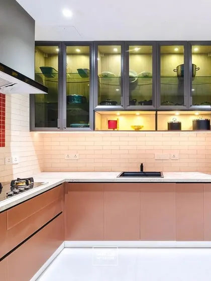 A showcase of bold design, this kitchen features a unique dusty rose and grey color scheme. The glass-front upper cabinets with internal lighting display crockery beautifully, while the integrated oven and hob create a seamless and highly functional cooking space.
