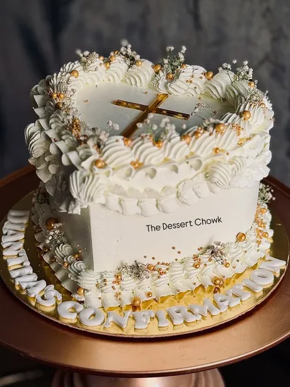 A heart-shaped cake with intricate vintage Lambeth piping, designed for a confirmation ceremony. The all-white design is pure and elegant.