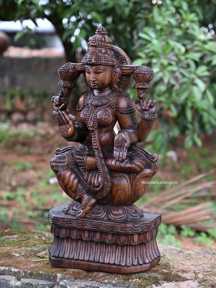 A 24-inch sculpture of Maha Lakshmi, carved with a fine wax brown finish and set in a natural environment.