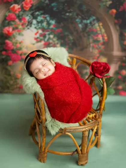 A sleeping beauty in a garden of roses. This newborn girl, wrapped in a vibrant red, looks so serene in this romantic and floral-themed setup.