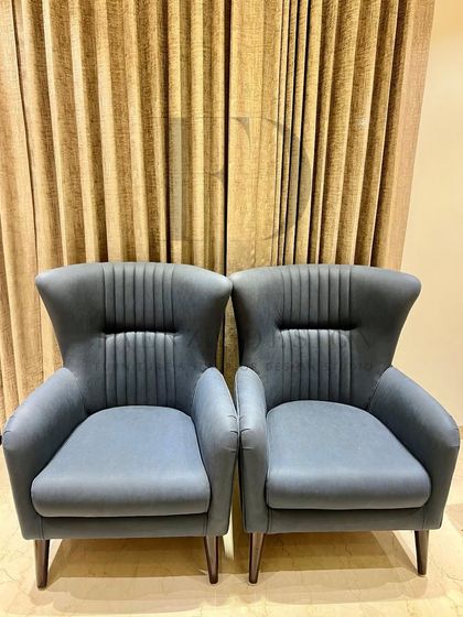 A pair of slate-blue high-back armchairs. The vertical channel tufting and winged design create a sense of modern elegance and provide comfortable, supportive seating.