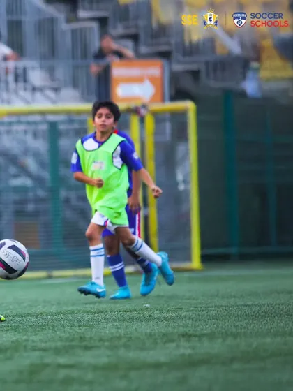 A young player in a green bib dribbling with purpose during a training game.