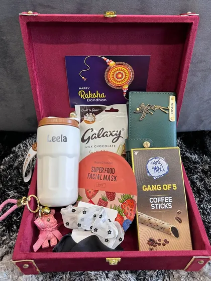 This Rakhi hamper for a sister is packed with self-care goodies. It includes a personalized tumbler and clutch, a face mask, coffee sticks, and chocolates, all presented in a luxurious velvet box.