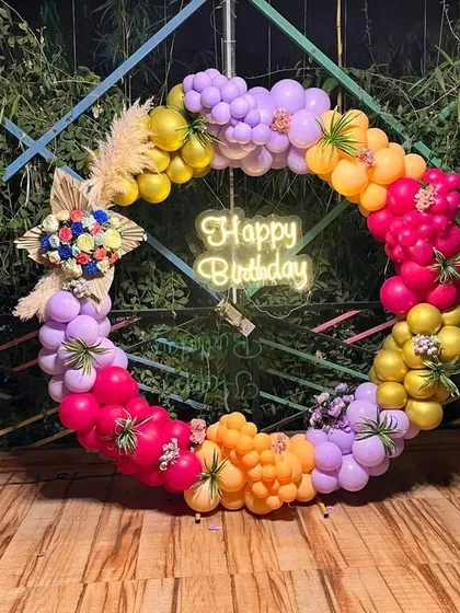 A colorful free-standing balloon ring with floral accents and a central neon sign, perfect as a mobile photo booth for any party.