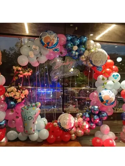 A full view of the red and blue baby shower decor. You can see the balloon columns topped with giant baby boy foil balloons, all framing a beautiful ring backdrop lit with fairy lights.