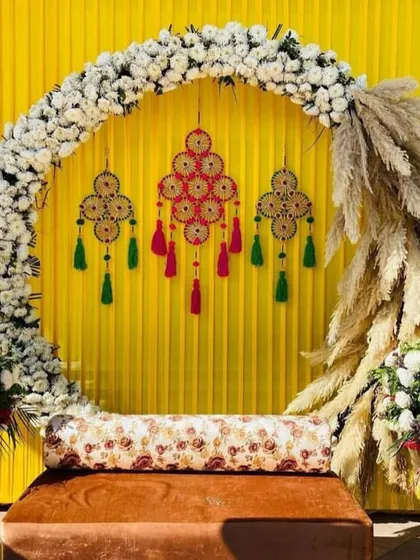 This is a popular setup for a Mehndi or Haldi ceremony. It combines a modern white floral arch with a traditional yellow backdrop and decorative hangings, creating a vibrant and stylish space for your pre-wedding functions.
