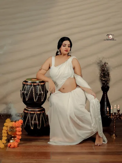 This portrait showcases the mother-to-be in a serene and powerful pose. She leans against traditional Indian drums (tabla), her white saree and exposed baby bump creating a look that is both artistic and culturally rooted.