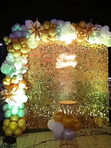 An outdoor party setup at night with a large golden sequin wall, creating a dazzling effect.