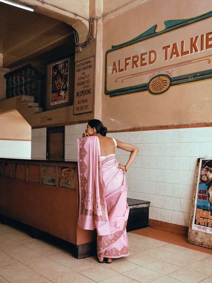 A woman in a pink Banarasi saree at the ticket counter of an old cinema hall. This scene for Tilfi's 'Banaras, Bombay' campaign evokes a sense of nostalgia and cinematic romance.