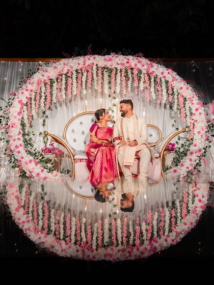 A stunning shot of the couple seated on a swing, surrounded by a circle of flowers, with their reflection in the floor below. This is a highly creative and beautifully composed reception photo.