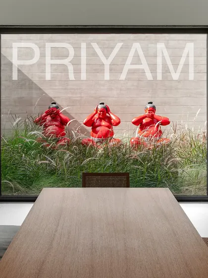 Three bright red sumo wrestler sculptures sit playfully among ornamental grasses. This installation, viewed from a dining room window, adds a bold pop of color and character to the minimalist landscape.