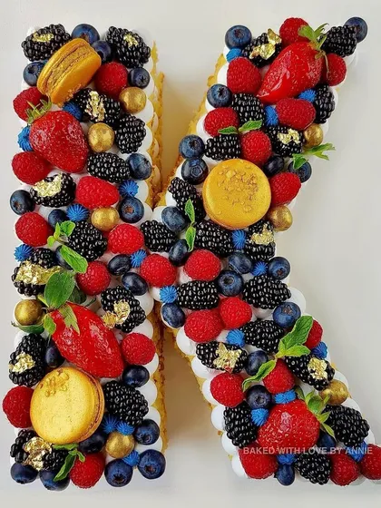 Another custom monogram cake, this time the letter 'K', adorned with fresh berries, macarons, and touches of gold leaf.