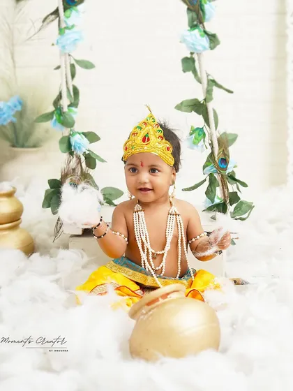 Our little Krishna is ready to play with a pot of delicious butter. The simple, bright setup with a floral swing keeps the focus on his adorable expression.