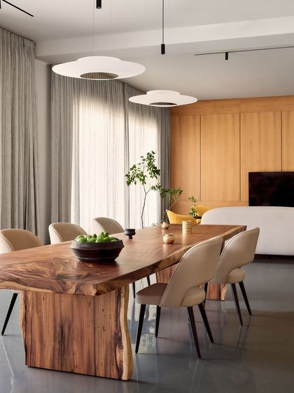 The elegant dining space at Amaiti Farmhouse, where a solid wood table is surrounded by contemporary chairs under soft, diffused lighting.