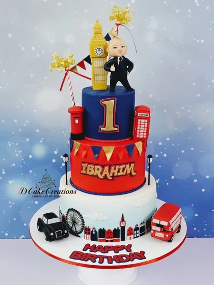 A three-tier London-themed cake for Ibrahim's first birthday, featuring a "Boss Baby" style figurine, Big Ben, and a classic red bus.