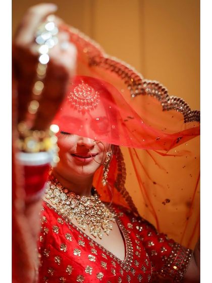 An artistic shot of a bride, her face partially obscured by her red veil.