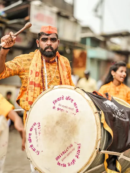 A dhol player with an intense gaze, his stick raised, ready to strike.