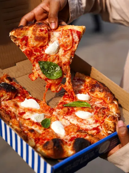A hand pulling a slice of cheesy Margherita pizza from the box. This classic "cheese pull" shot is incredibly appetizing and a must-have for any pizza brand's social media.