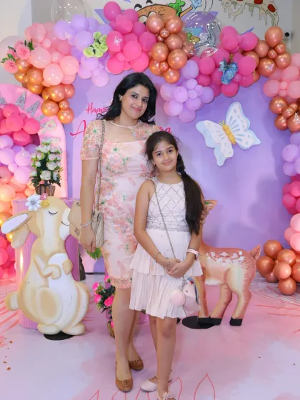 A mother and daughter in front of a whimsical woodland creature and butterfly-themed backdrop. The soft colors and cute animal props are perfect for a gentle, nature-inspired party.