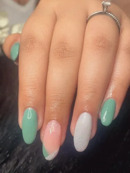 A soft, sage green French manicure with a mix of solid colors and glitter accents.