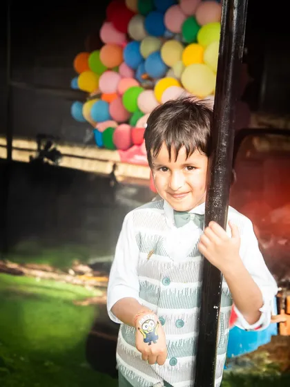 The birthday boy, looking dapper in his vest, peeks out from behind a pole. A playful, candid moment captured during his party.