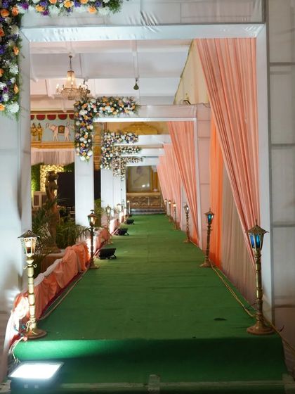 I designed this long walkway with a green carpet, lined with peach-colored drapes and traditional Indian-style lamps. Floral arrangements are placed along the pillars to enhance the grand feeling of the entrance.