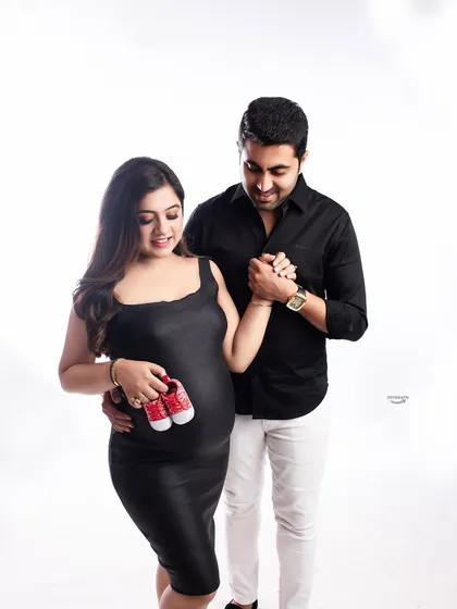 A sweet and classic couple pose, holding hands and a tiny pair of red baby shoes. The simple black and white outfits against a clean background make this a timeless memory.