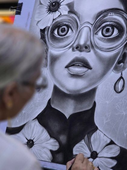 A closer look at the charcoal portrait in progress. The artist is adding details to the clothing and background, building up layers to create a complete and compelling image.