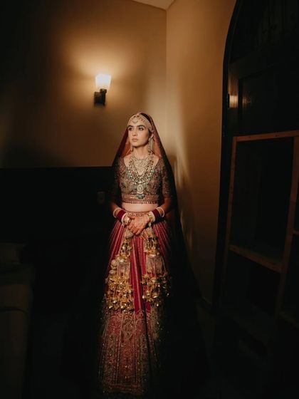 A full-length portrait of the bride standing in a dimly lit hallway, her regal presence and stunning lehenga creating a powerful image.