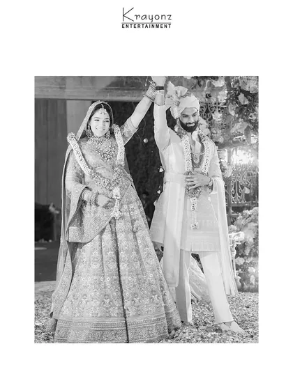 A timeless black and white portrait of the newly married couple, celebrating their union with hands raised in joy. This classic shot captures the pure happiness of the moment.