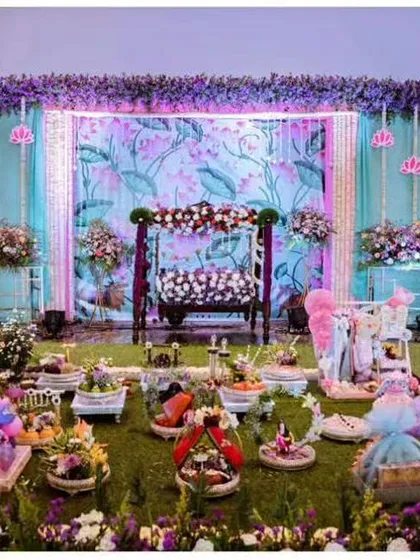 I love creating dreamy baby shower setups like this one. It features a decorative jhoola, or swing, set against a pastel floral backdrop, with an array of themed gift trays and decor spread across an artificial grass floor for a garden-like feel.