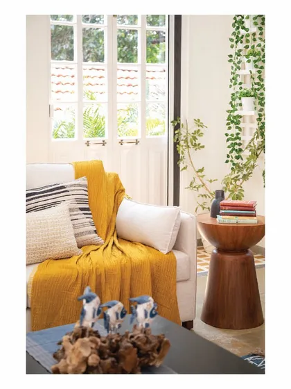 Another view of a warm corner space in the Goa villa. A comfortable sofa is dressed with a bright yellow throw and patterned cushions, set against a window that lets in the beautiful tropical light. These spaces are designed for unwinding and enjoying the slow pace of holiday life.